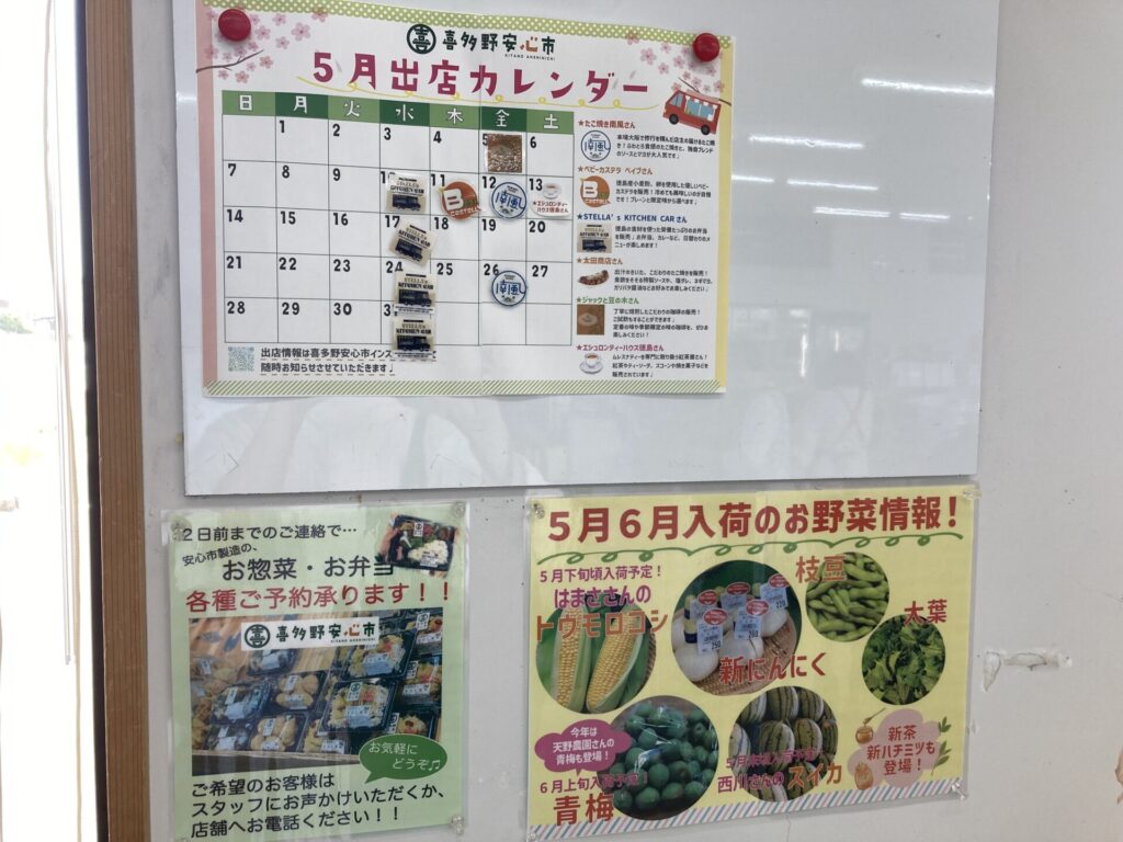 5月の出店カレンダーとお野菜情報、お弁当の予約チラシが貼られた掲示板